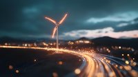 Glowing wind turbine against dramatic evening sky with light trails from traffic creating curved path, moody atmosphere and bokeh effect in foreground.