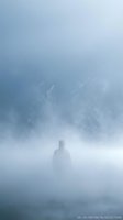 Solitary figure standing in dense fog with mountain peaks emerging from mist, conveying isolation, mystery, and contemplation. Suitable for mental health, existential themes, and atmospheric storytelling.