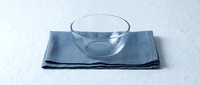 Clear glass bowl placed on folded blue linen napkin against white surface, suitable for food styling, tableware design, and kitchen product photography.