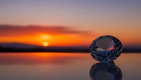 Crystal diamond reflecting sunset colors on water surface with dramatic orange and purple sky creating luxury jewelry concept for premium design projects.