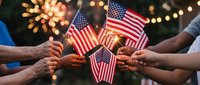 Diverse hands holding American flags together during patriotic celebration with fireworks and festive lights creating unity and national pride atmosphere.