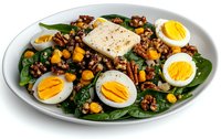 Fresh spinach salad with quinoa, halved boiled eggs, chickpeas, and feta cheese on white ceramic plate, garnished with black pepper and olive oil dressing.