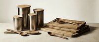 Modern kitchen storage set with stainless steel canisters and wooden lids alongside natural wood cutting boards and utensils on neutral background.