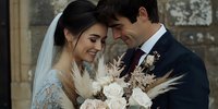 Romantic newlywed couple sharing intimate moment, bride holding bouquet with roses and pampas grass, groom in dark suit with boutonniere.