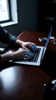 Professional businessman hands typing on laptop computer at wooden desk in modern office workspace for remote work and business productivity.