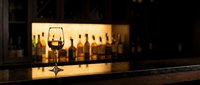 Wine glass on dark bar counter with blurred bottles and warm lighting in background creating elegant restaurant atmosphere for hospitality design.