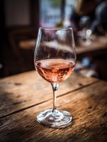 Rose wine glass on wooden table in restaurant setting with warm ambient lighting and blurred background creating elegant dining atmosphere.