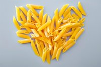 Raw penne pasta arranged in heart shape on gray background, perfect for food blog, restaurant menu, or cooking website design. Creative culinary concept.
