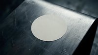 Blank white circular sticker label on dark scratched metal surface for branding mockup and product presentation design projects.