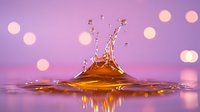 Liquid crown splash with droplets frozen in motion against purple and pink bokeh background, creating magical atmosphere in macro photography.