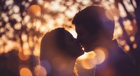 Romantic couple silhouettes kissing at sunset with warm golden bokeh lights creating intimate atmosphere for love and relationship concepts.