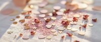 Scattered rose gold and copper sequins with glitter creating sparkly confetti pattern on soft fabric surface for crafting and party decoration projects.