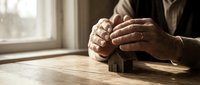 Businessman hands protecting wooden house model on desk symbolizing home insurance, real estate investment and property protection concept.