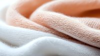Soft cotton fabric texture in gentle peach and white colors with delicate folds creating smooth waves and shadows, macro photography for fashion and textile design.