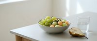 Young woman with fair complexion enjoying fresh green grapes and pear from ceramic bowl on white table with glass of water for healthy eating and nutrition lifestyle content.