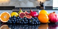 Fresh seasonal fruits arranged on dark reflective surface including grapes, oranges, figs, and pomegranate creating colorful healthy food composition.