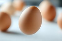 Fresh brown chicken egg floating in air against blurred background of other eggs, soft focus macro photography with selective depth of field.