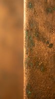 Rusty metal pipe with green corrosion spots and oxidation damage showing weathered industrial surface texture in warm lighting for maintenance concepts.