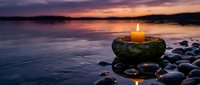 Peaceful candle flame glowing on stacked stones by tranquil lake at sunset, creating serene meditation and wellness atmosphere for relaxation and mindfulness.