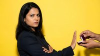 Professional Hispanic businesswoman in dark suit refusing alcohol with stop gesture against bright yellow background for workplace wellness campaigns.