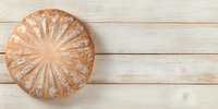 Freshly baked round artisan bread loaf with decorative scoring pattern on rustic wooden table, perfect for food photography.