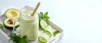 Fresh green smoothie with avocado and cucumber in glass jar with bamboo straw on white wooden tray, healthy detox drink for wellness lifestyle.