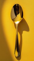 Shiny silver spoon casting dramatic shadow on vibrant yellow background. Minimalist food photography with strong contrast and clean lines for culinary content.