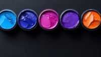 Vibrant powder pigments in blue, purple, pink and orange shades arranged in round containers on dark background, showing texture and intensity of pure color.