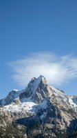 Dramatic snow-capped mountain peak with jagged rocky summit against clear blue sky and white clouds. Alpine landscape for travel, nature, and outdoor adventure projects.