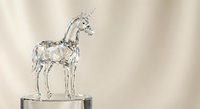 Crystal glass unicorn figurine with spiral horn standing on reflective surface against soft beige background for luxury home decor and collectibles.