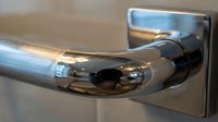 Modern chrome door handle with sleek curved design mounted on square backplate, polished metal hardware for contemporary interior doors and home renovation.