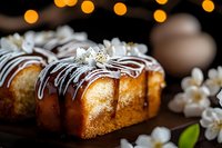 Freshly baked pound cake with white chocolate drizzle and spring cherry blossoms on dark wooden surface against blurred golden bokeh background.