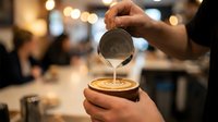 Barista pouring steamed milk into a latte art coffee cup in a modern cafe, creating a delicate floral pattern on the surface.