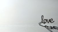 Handwritten word love in elegant cursive script on clean white paper background with soft shadows creating romantic minimalist composition.