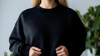 Young Caucasian woman in black oversized sweatshirt standing against blurred green plant background, minimalist casual fashion lifestyle portrait.