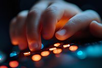 Close-up of fingers touching illuminated control panel buttons with orange and blue backlighting against dark background, creating modern technological ambiance.