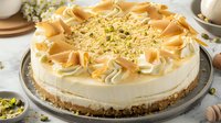 Creamy no-bake cheesecake topped with caramel swirls and crushed pistachios on graham cracker crust, served on gray plate against light background.