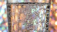 Sparkling water glass with bubbles and condensation droplets against colorful bokeh background for refreshment and beverage concepts.