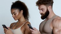 Young African American woman and Caucasian bearded man looking at their smartphones, standing close together against white background, modern lifestyle concept.