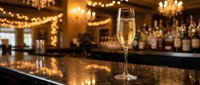 Elegant champagne flute filled with sparkling wine on polished bar counter with warm bokeh lights and upscale restaurant atmosphere for celebrations.