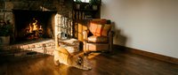 Cozy living room interior with crackling fireplace, leather armchair and warm golden lighting creating comfortable home atmosphere for relaxation.