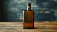 Vintage amber glass bottle on rustic wooden surface against moody dark background. Atmospheric still life photography with antique apothecary or medicine container.