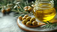 Fresh green olives and golden olive oil in glass jar on wooden plate with olive branches for Mediterranean cooking and healthy nutrition.