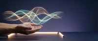Human hands cupping glowing energy waves with flowing light streams above palms against dark background for wellness and spiritual concepts.