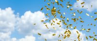 Golden confetti falling from bright blue sky with fluffy white clouds creating celebratory atmosphere for success and achievement concepts.