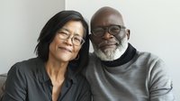 Mature diverse couple smiling together, showcasing genuine connection and companionship against neutral background.