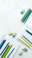 Colorful pencils and erasers arranged on white background with grid paper for creative projects and educational activities.