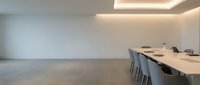 Modern minimalist conference room with long wooden table, gray chairs, and recessed ceiling lighting in empty corporate space.