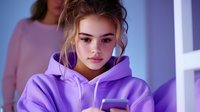 Young woman in purple hoodie using smartphone with soft purple lighting, casual lifestyle portrait showing modern technology and youth culture.