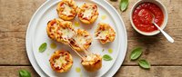 Mini pizza bites with melted cheese and herbs on white plate, served with marinara sauce on rustic wooden table for appetizers and party snacks.